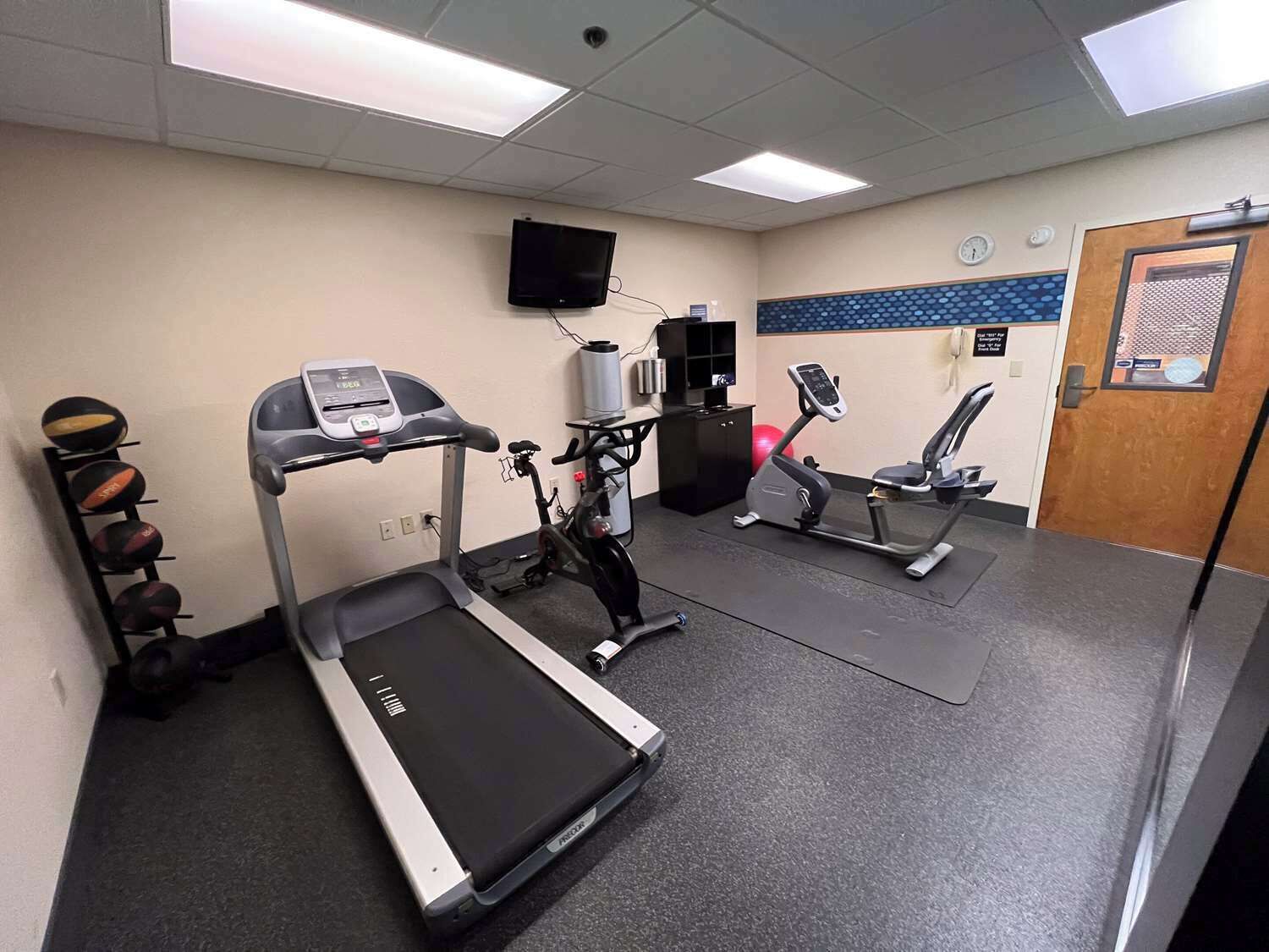 A gym with a treadmill, elliptical, stationary bike, and a wall-mounted TV.