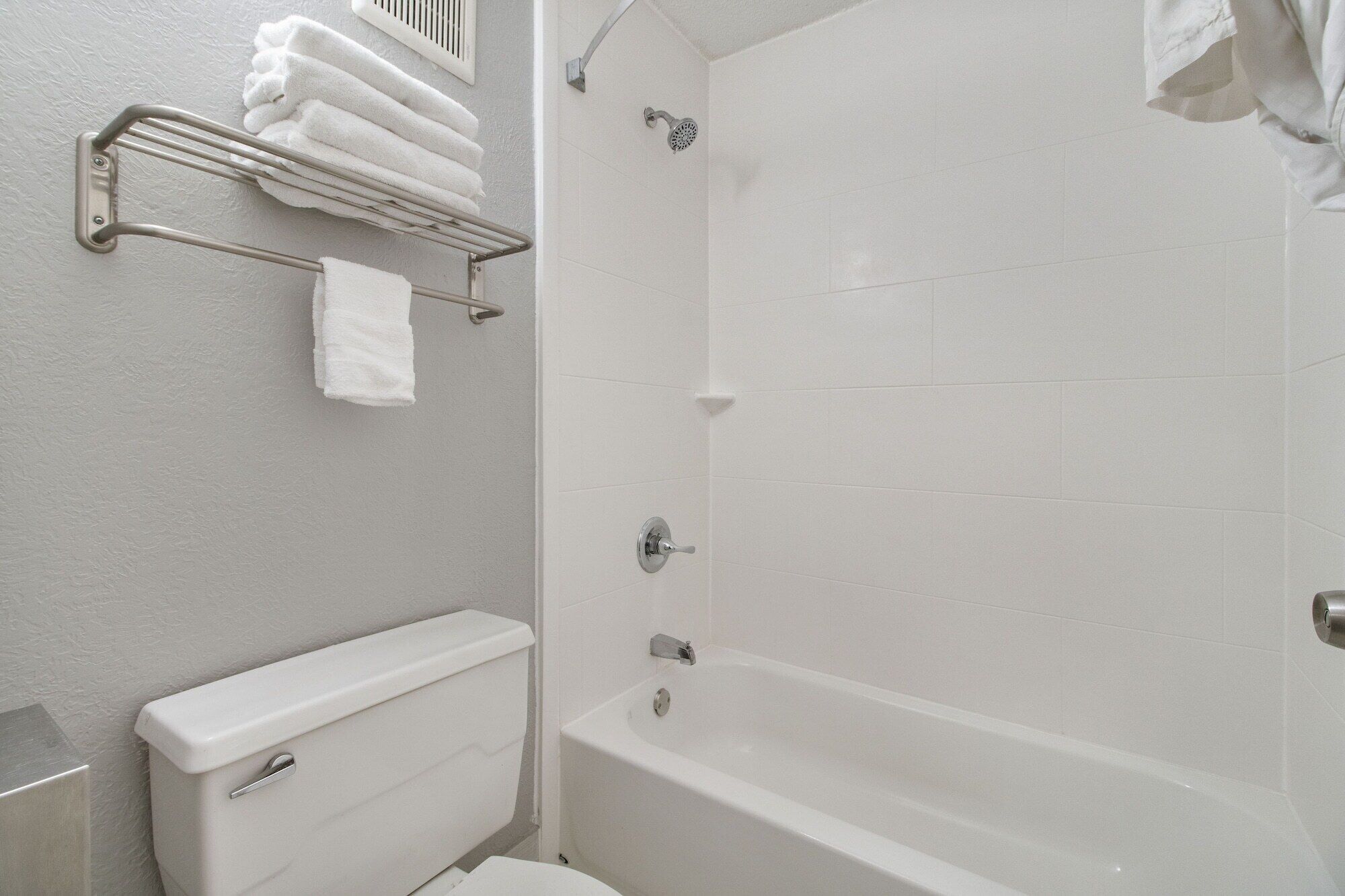 A bathroom with a toilet, a shower, and a towel rack with folded towels.