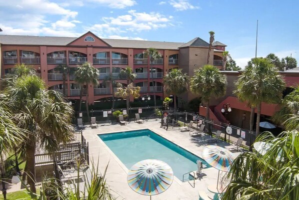 A hotel with a swimming pool, palm trees, and a multi-story building with balconies. - Beachfront Palms Resort Galveston, an Ascend Collection Hotel (Galveston)