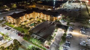 An aerial view of a hotel with multiple floors, a parking lot, and surrounding greenery. - Beachfront Palms Resort Galveston, an Ascend Collection Hotel (Galveston)