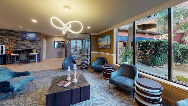 A modern hotel lobby with a stone wall, a reception desk, seating area, and large windows offering a view of the outdoors. - Beachfront Palms Resort Galveston, an Ascend Collection Hotel (Galveston)