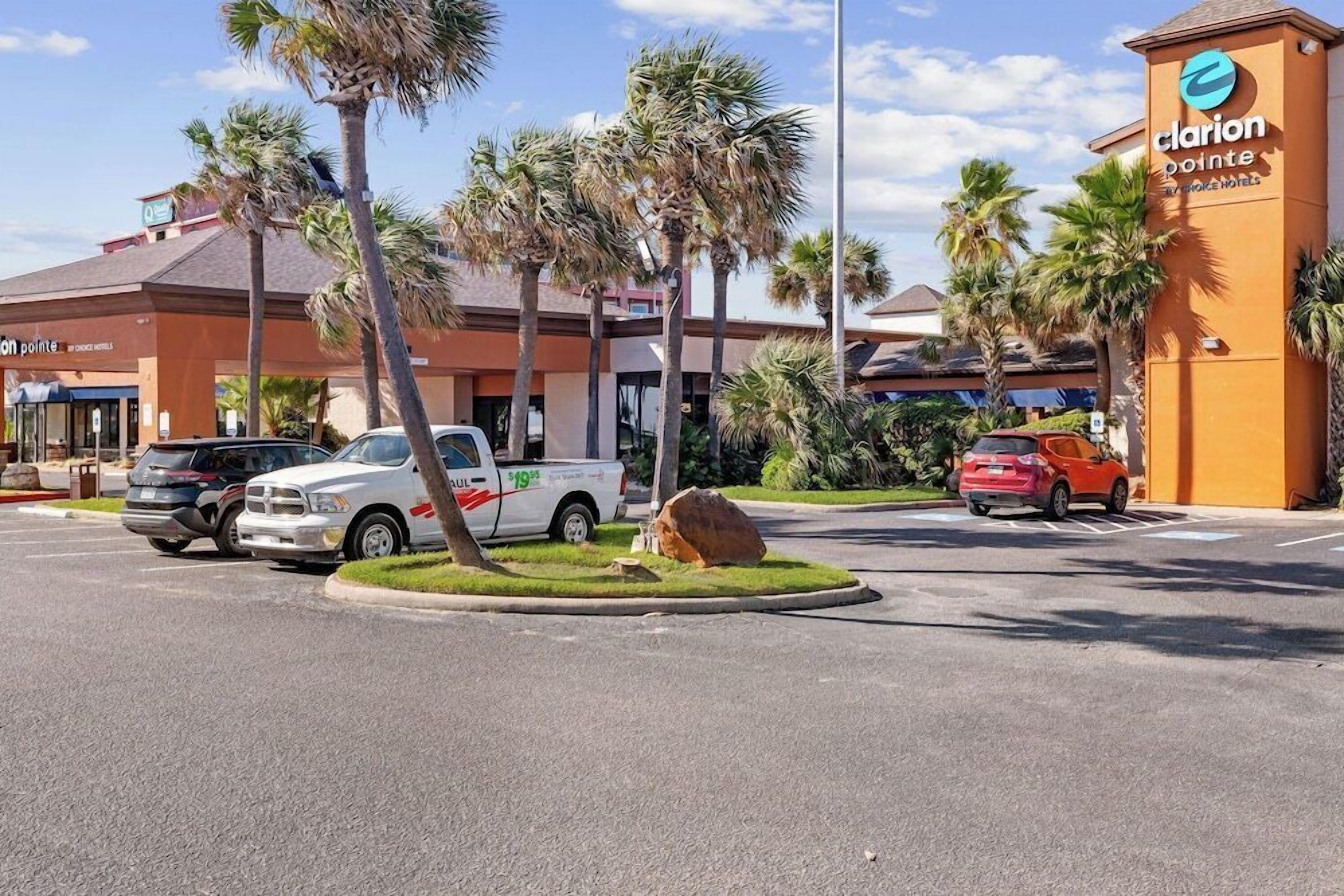 A parking lot with several vehicles, palm trees, and a building with a sign for Clarion Pointe Hotel.