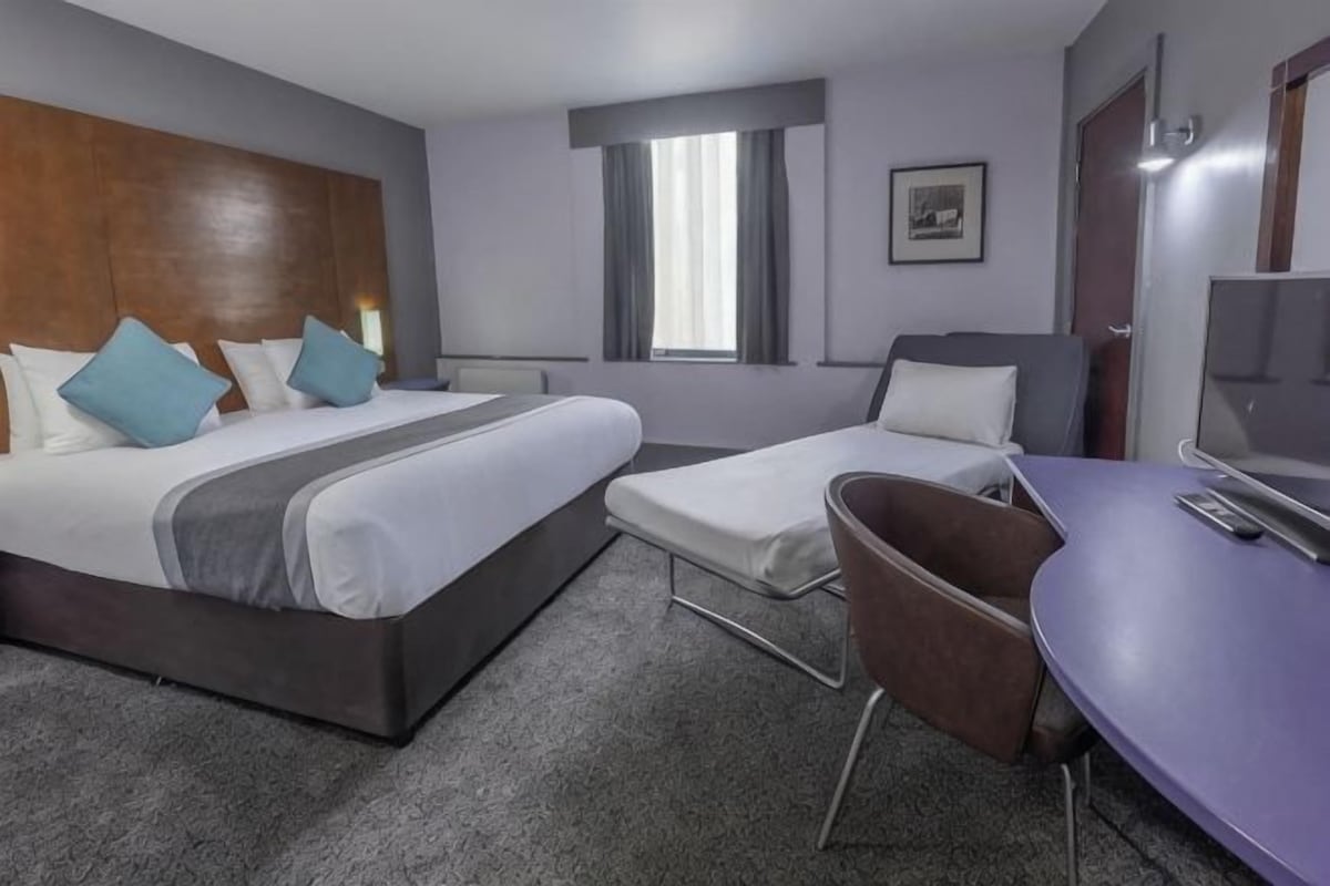 A hotel room with a large bed, a smaller bed, a desk, and a chair.