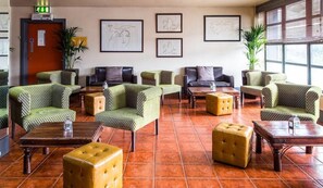 A lobby with green patterned sofas, wooden tables, and a tiled floor.