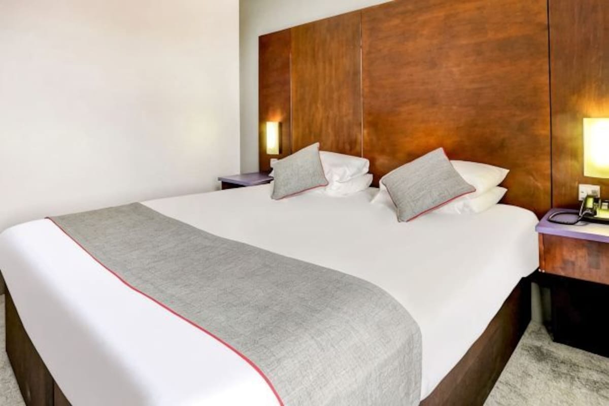 A hotel room with a large bed, wooden headboard, bedside lamps, and a bedside table.