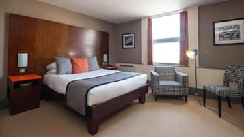Ein Hotelzimmer mit einem großen Bett, zwei Nachttischen, einem Sessel, einer Lampe und einem Fenster mit Vorhängen.