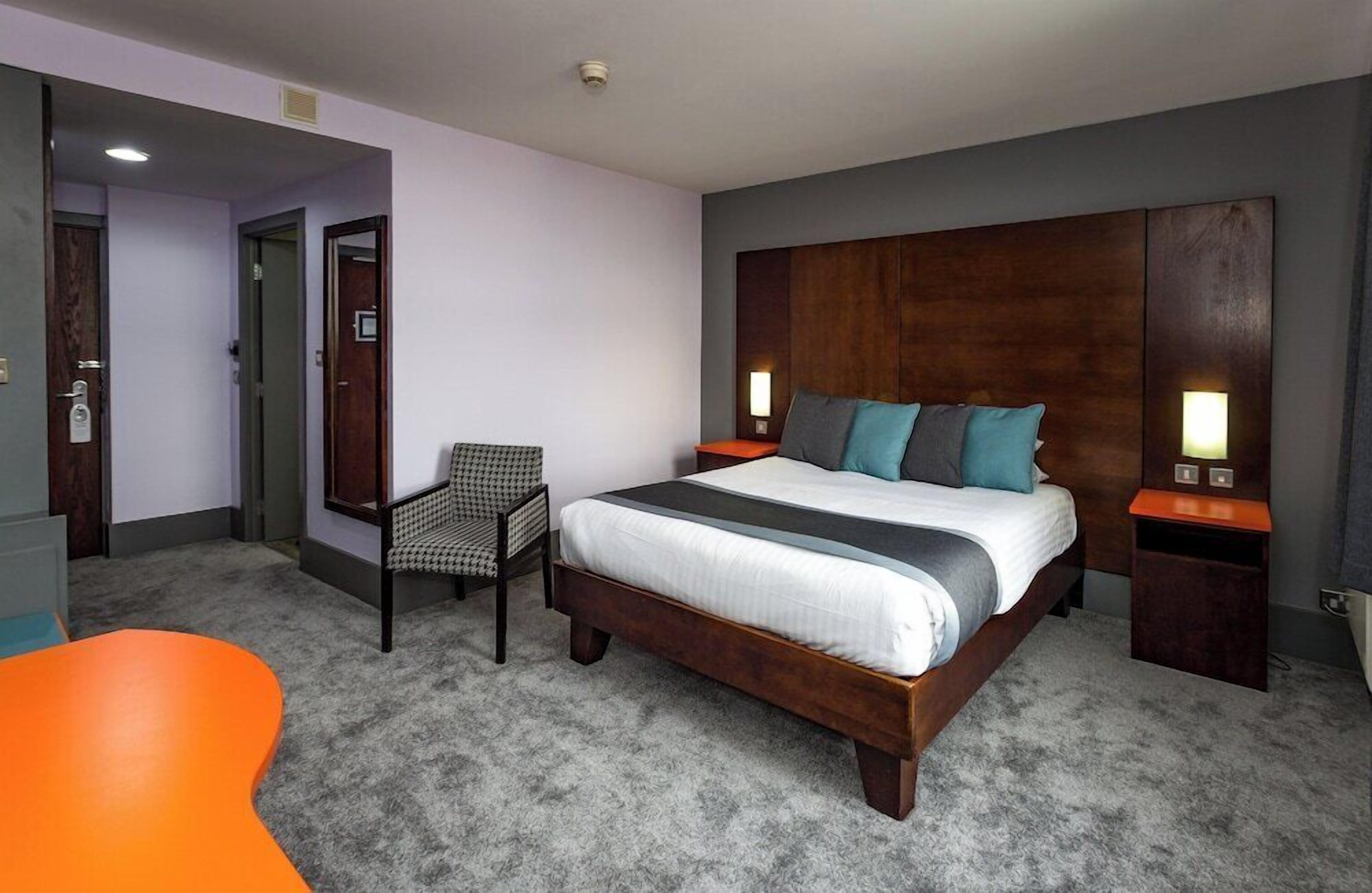 A hotel room with a large bed, a chair, a small table, and two bedside lamps.