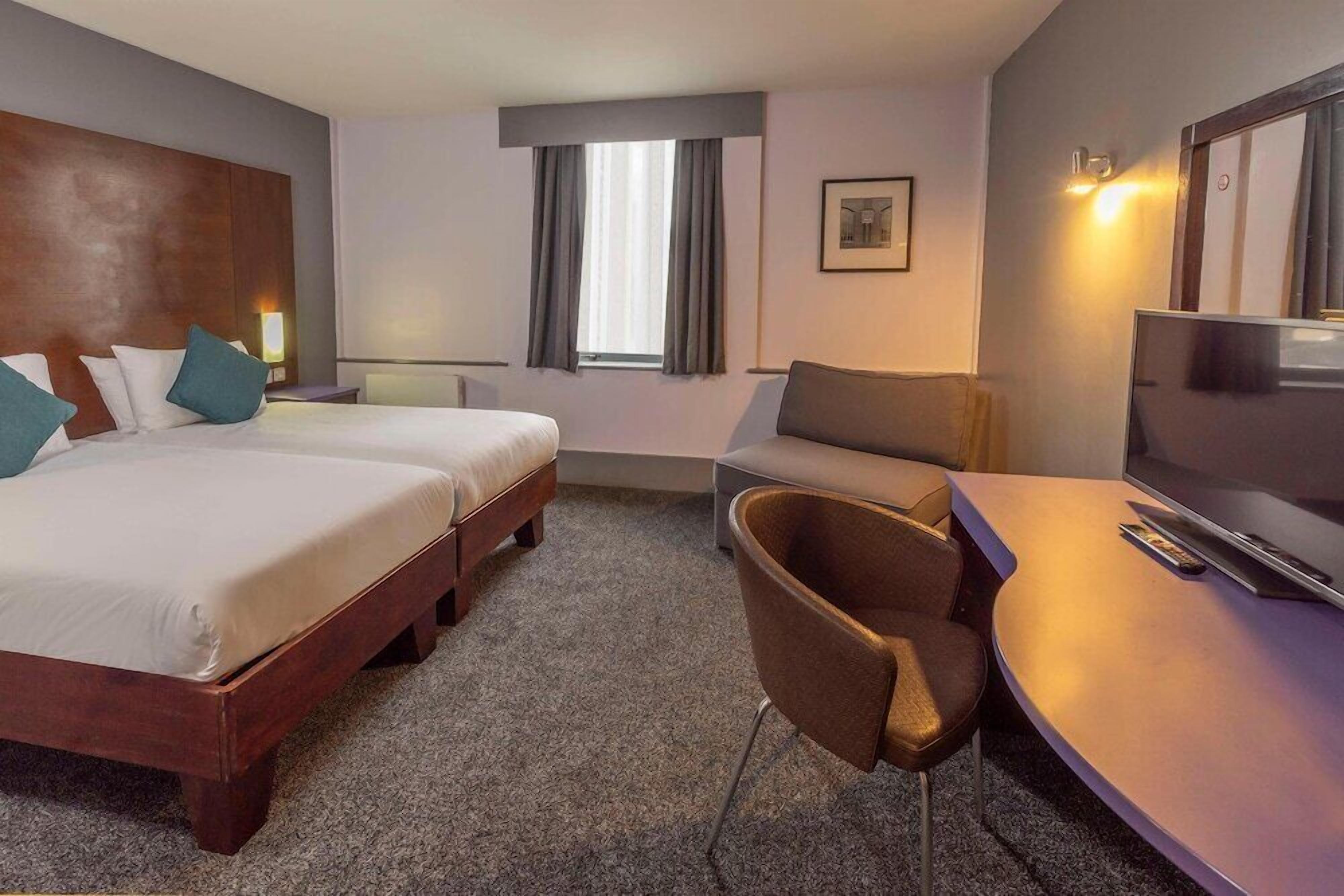 A hotel room with two beds, a TV, a desk, and a chair.