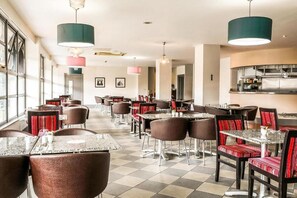 Un restaurante con varias mesas y sillas, una zona de cocina e iluminación colgante.