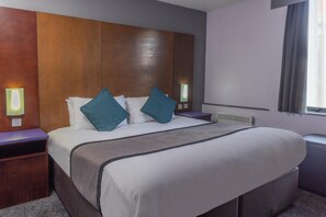 Una habitación de hotel con una cama grande, dos mesitas de noche, un cabecero y una ventana con cortinas.