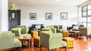 A lobby with green patterned chairs, a black sofa, and a yellow ottoman. There are framed pictures on the wall and a door with an emergency exit sign. - Sheffield Metropolitan Hotel by Belvilla (Sheffield)