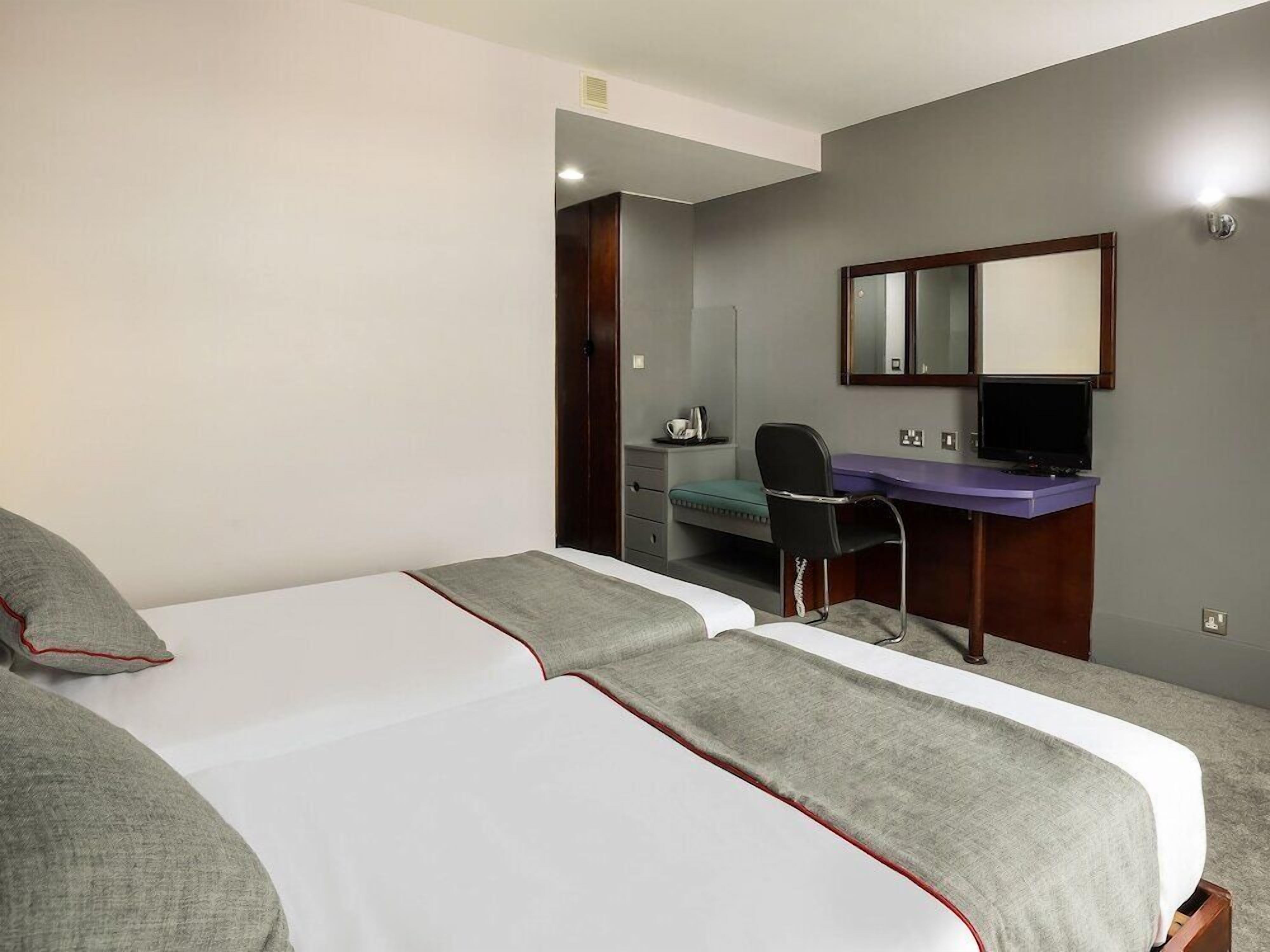 A hotel room with a bed, a desk, a chair, a mirror, and a television.