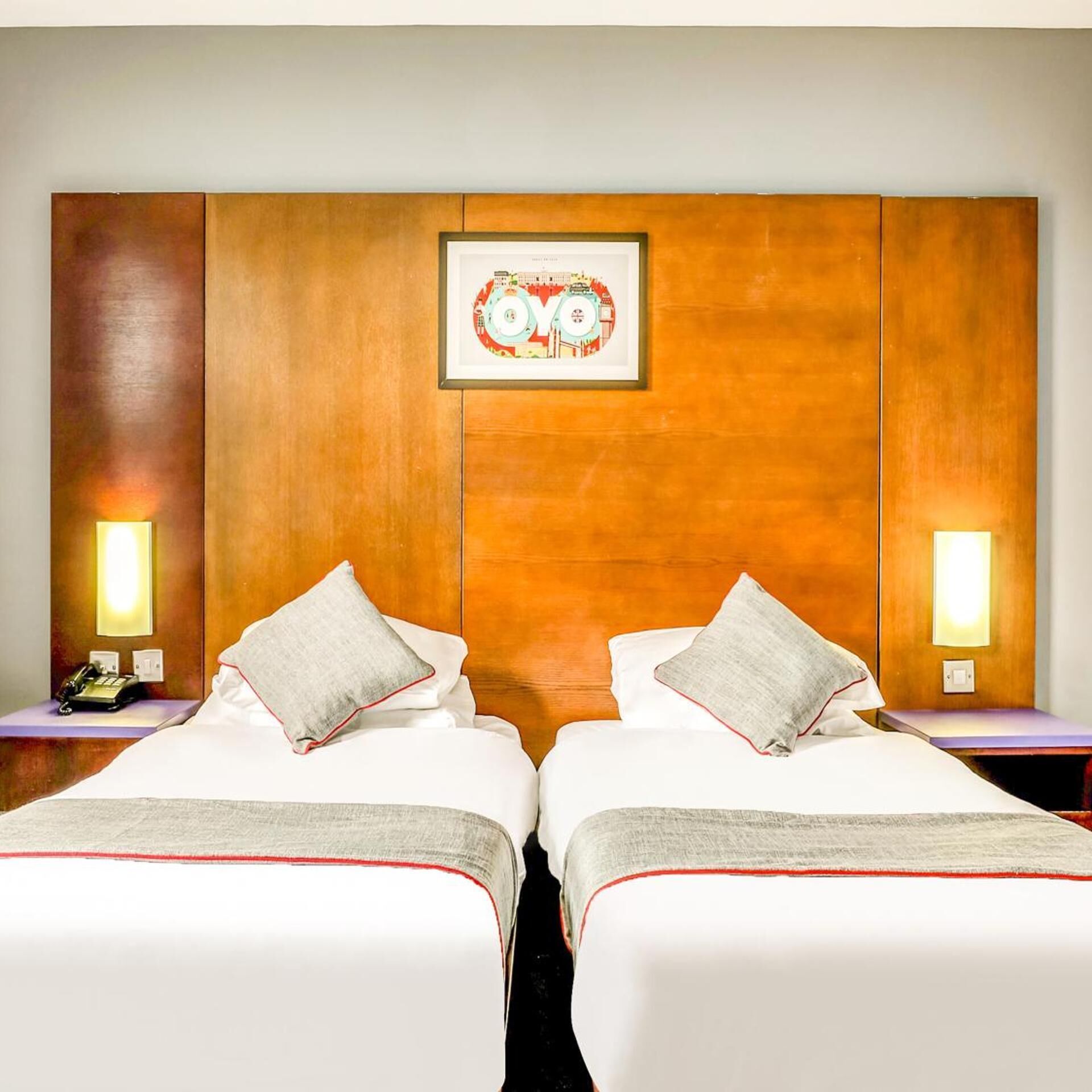Ein Hotelzimmer mit zwei Betten, einem Holzkopfende, einem gerahmten Bild, Nachttischlampen und einem Telefon auf dem Nachttisch.