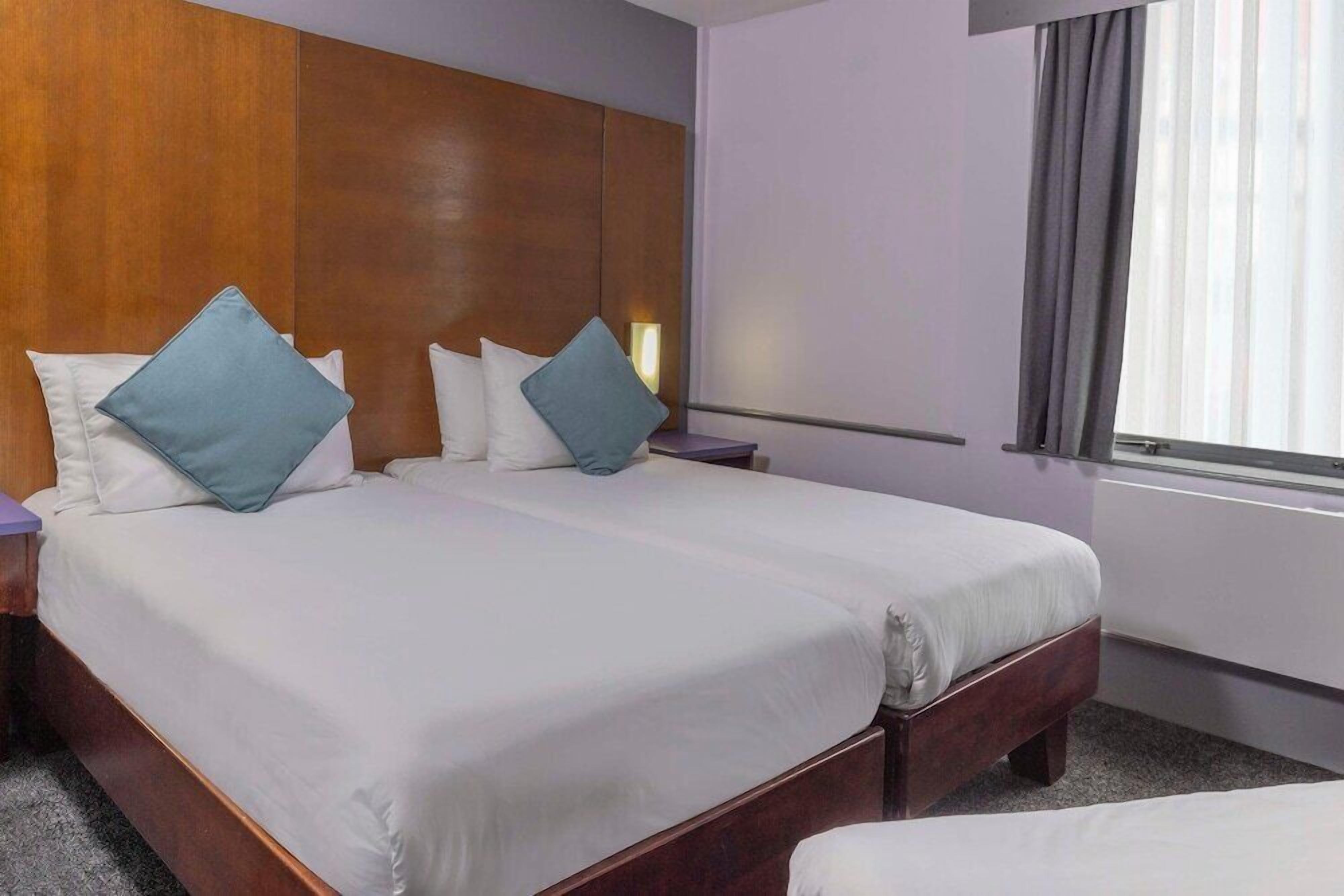 A hotel room with two beds, wooden headboard, white bedding, and a window with curtains.