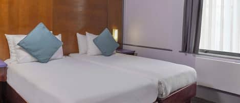 A hotel room with two beds, wooden headboard, white bedding, and a window with curtains.