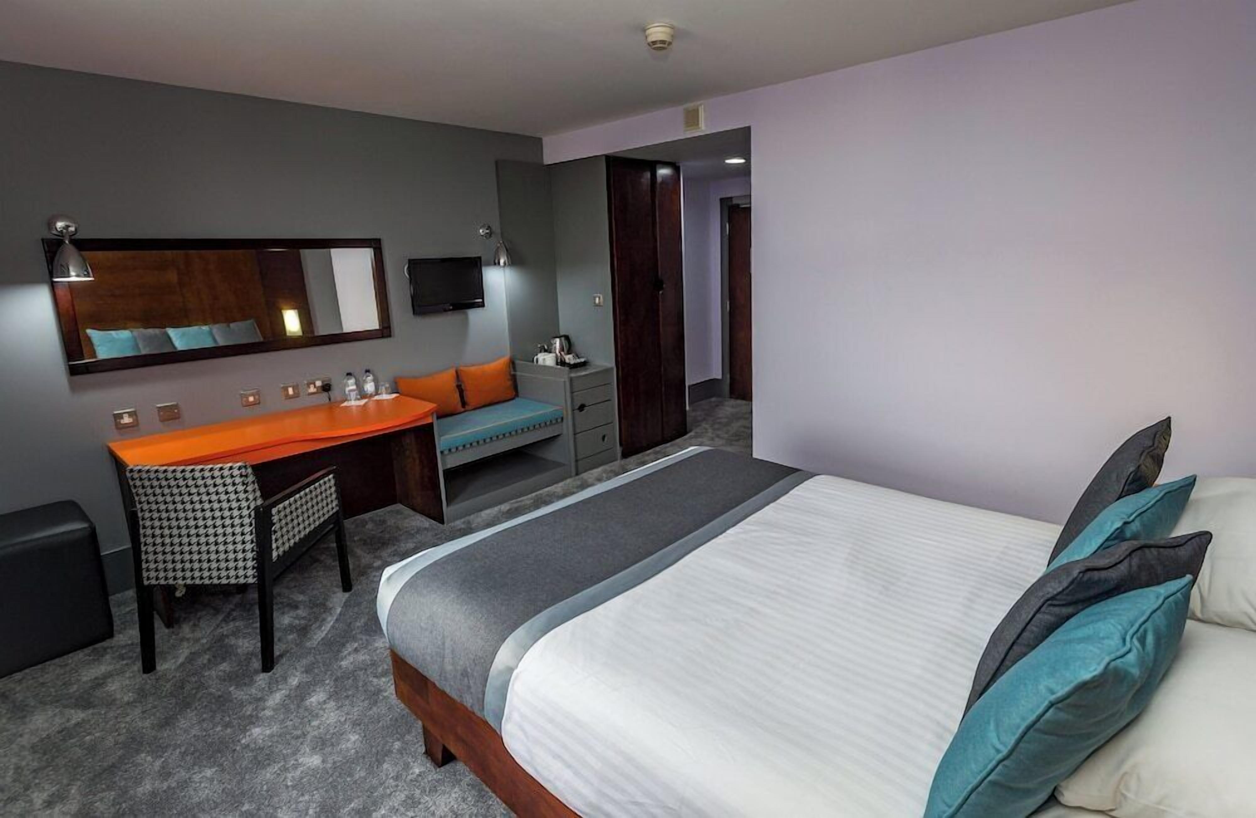 A hotel room with a bed, a desk, a chair, a mirror, and a television.