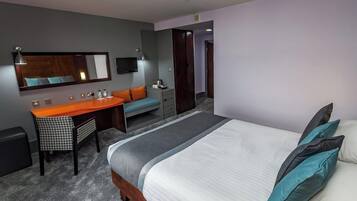 A hotel room with a bed, a desk, a chair, a mirror, and a television.