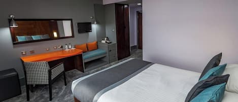 A hotel room with a bed, a desk, a chair, a mirror, and a television.