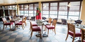 A spacious restaurant with multiple tables and chairs, large windows with blinds, and potted plants. - Sheffield City Hotel (Sheffield)