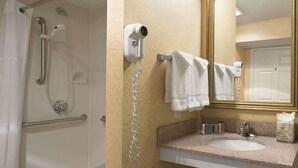 A bathroom with a shower, a hairdryer, a towel rack, a sink, and a mirror. - Suburban Studios Fort Wayne, IN (Fort Wayne)