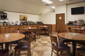 Un comedor con mesas y sillas redondas, una estación de café y un televisor montado en la pared.