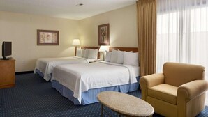 A hotel room with two beds, a chair, a table, and a TV. - Suburban Studios Fort Wayne, IN (Fort Wayne)