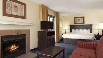 A hotel room with a fireplace, a bed, a desk, a TV, and a large window.