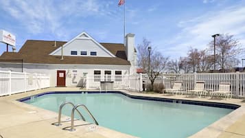 A swimming pool with a white fence, a flag, and a building with a sign.