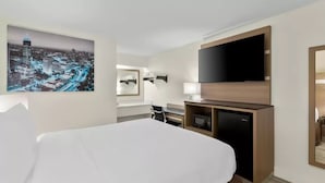 A hotel room with a bed, a flat-screen TV, a desk with a lamp, a microwave, and a cityscape painting. - Clarion Pointe Kennesaw Town Center (Kennesaw)
