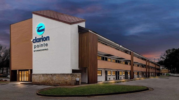 A hotel with a modern design, featuring a prominent logo on the facade, multiple floors, and a parking lot. - Clarion Pointe Kennesaw Town Center (Kennesaw)