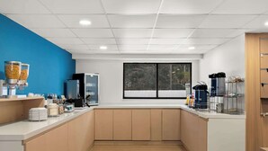 Een moderne keuken met een blauwe accentmuur, een groot raam en diverse apparaten.