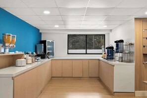 A modern kitchen with a blue accent wall, a large window, and various appliances. - Clarion Pointe Kennesaw Town Center (Kennesaw)