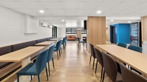A modern dining area with long tables and chairs, a wooden partition, and a view of the outdoors. - Clarion Pointe Kennesaw Town Center (Kennesaw)