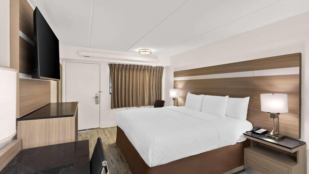 Een hotelkamer met een bed, nachtkastje, lamp, televisie en een bureau met stoel.