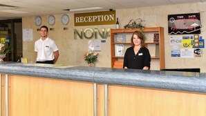 Un mostrador de recepción con un letrero que dice 'RECEPTION NONA', un reloj y una pantalla digital que muestra la hora y la fecha.