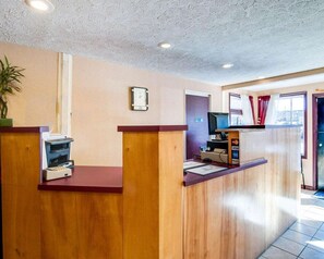 A reception area with a wooden counter, a clock, a computer, and a window with curtains. - Econo Lodge Galax, VA (Galax)