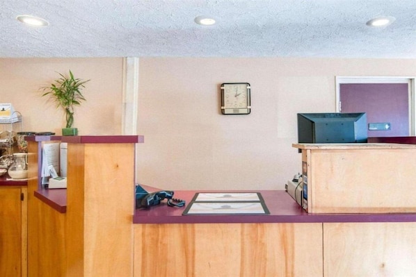 Una recepción con un reloj, una planta y un televisor sobre un pedestal.