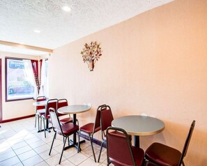 A dining area with round tables and red chairs, a decorative wall piece, and a window with a sign. - Econo Lodge Galax, VA (Galax)