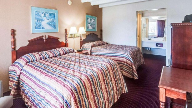 A hotel room with two beds, a wooden headboard, a small table, and a mirror. - Econo Lodge Galax, VA (Galax)