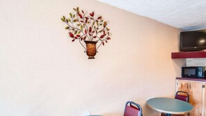 A room with a round blue table, red chairs, a wall-mounted decorative piece, and a microwave on a wooden cabinet. - Econo Lodge Galax, VA (Galax)