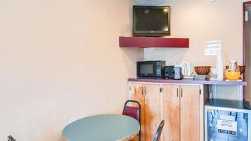 A small kitchenette with a microwave, toaster, and coffee maker on the counter, a television above, and a water dispenser on the right.