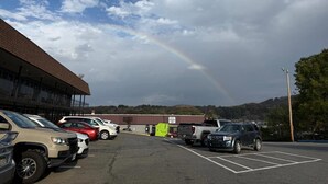 A parking lot with vehicles, a building with a sign, and a rainbow in the sky. - Econo Lodge Galax, VA (Galax)