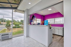 A reception area with a glass door leading outside, a counter with a computer, and a purple wall. - Motel6 Tuscaloosa, AL University (Tuscaloosa)