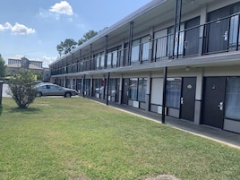 A multi-story motel with a flat facade, large windows, and a parking area in front.