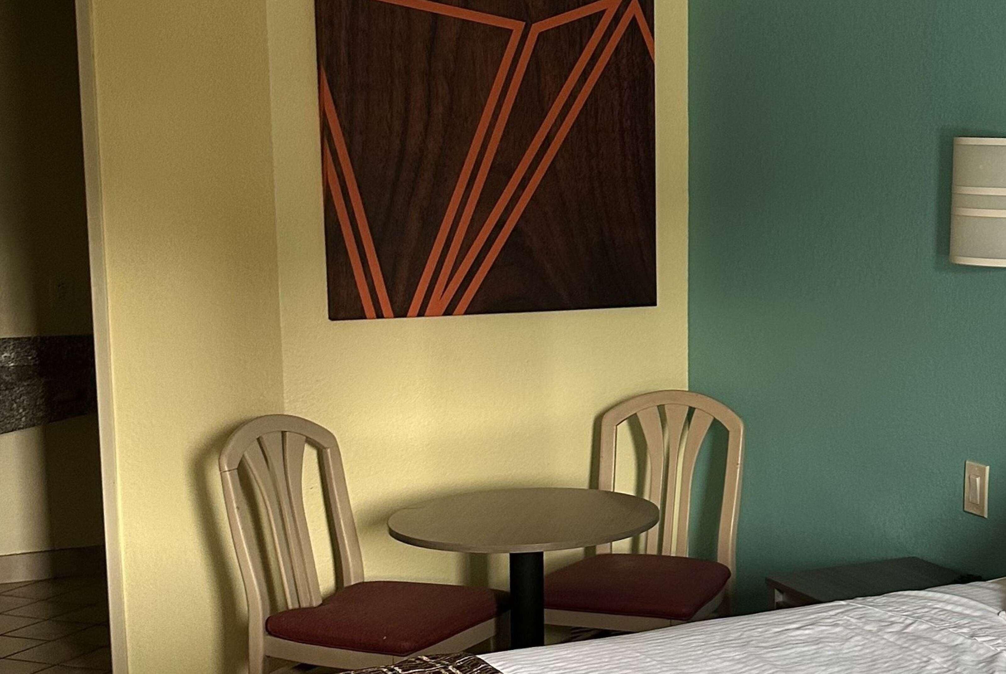 A hotel room with a bed, two chairs, a small table, and a wall-mounted light fixture.