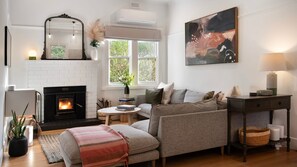 A living room with a fireplace, sofa, coffee table, and artwork. - Higgins House - Hepburn Springs (Hepburn Springs)