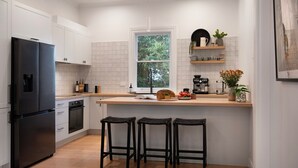 Een moderne keuken met een zwarte koelkast, witte kasten, een raam met uitzicht op groen, een koffiezetapparaat en drie zwarte barkrukken.