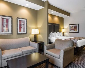 A hotel room with a sofa, armchair, a bed, a nightstand, and a lamp. - Red Roof Inn and Suites Longview (Longview)
