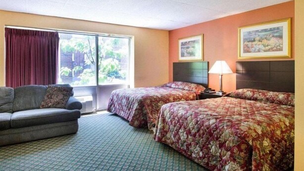 A hotel room with two beds, a sofa, a window with curtains, and two framed pictures on the wall. - Econo Lodge Framingham (Framingham)