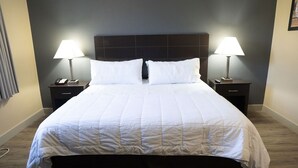 Una cama bien hecha con edredón blanco, dos mesitas de noche con lámparas y un cabecero oscuro.